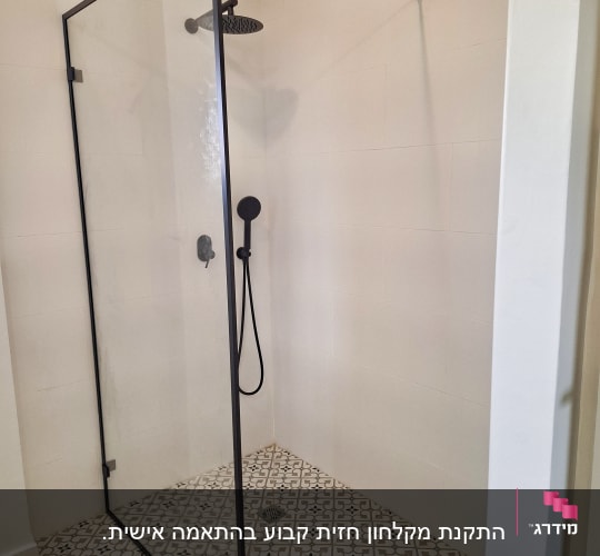מקלחון זכוכית עם ראש מקלחת שחור על רצפת אריחים מעוצבת